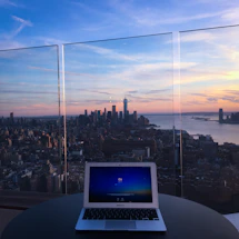 Elegant workspace with a laptop, travel brochures, and a cup of coffee beside a window overlooking a city skyline at sunset.