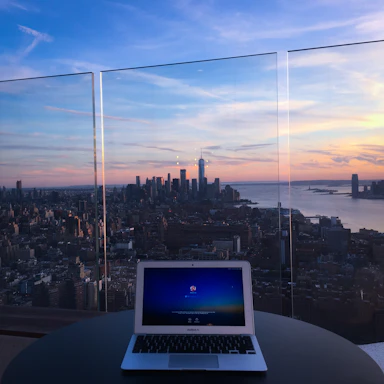 Elegant workspace with a laptop, travel brochures, and a cup of coffee beside a window overlooking a city skyline at sunset.