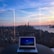 Photo of a confident businessman using a laptop with a city skyline in the background.