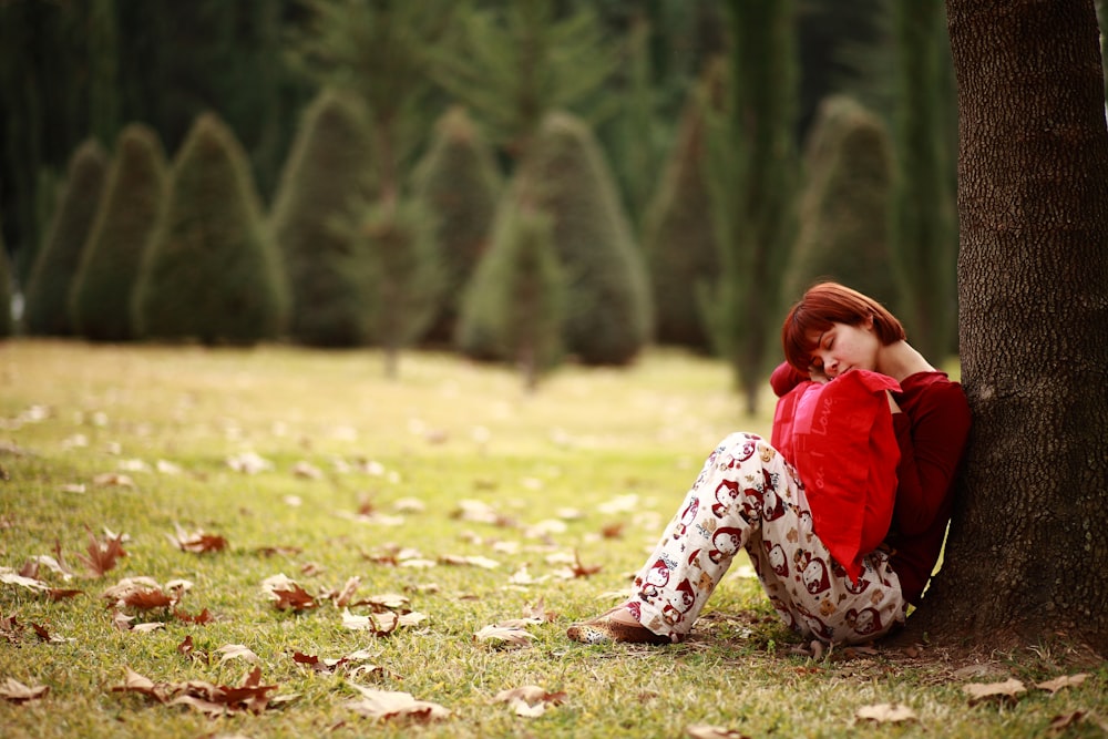 girl in red shirt and white and black pants sitting on green grass field during daytime