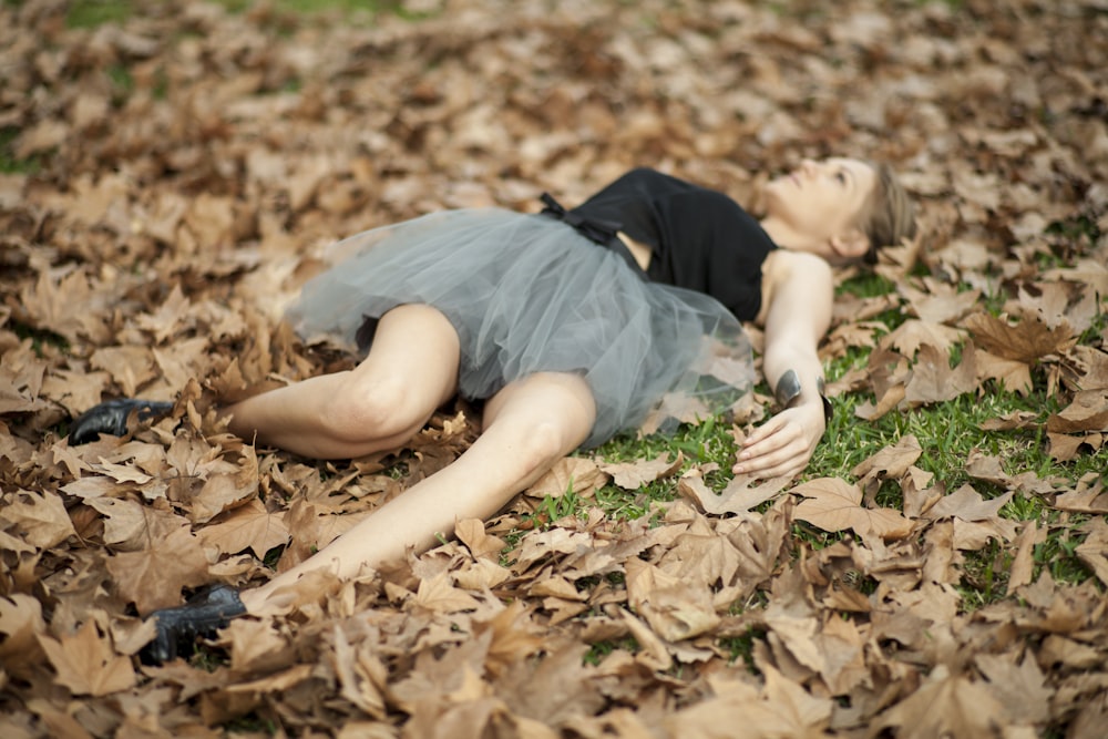 woman in gray dress lying on dried leaves