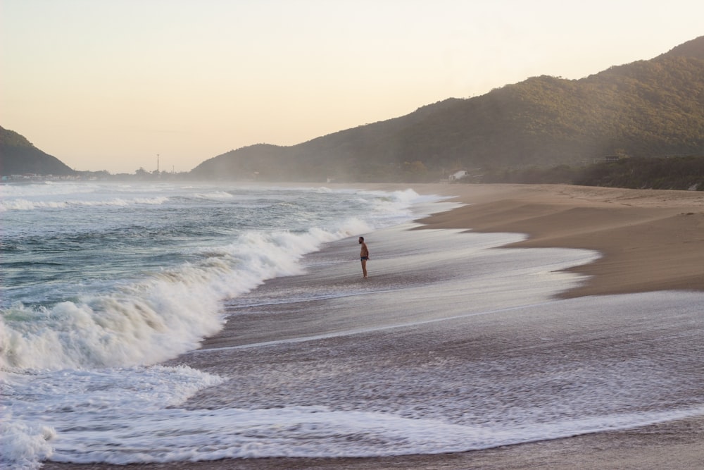 person in red shirt standing on seashore during daytime