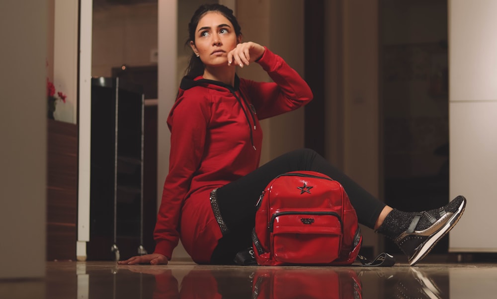 woman in red leather jacket sitting beside red leather backpack