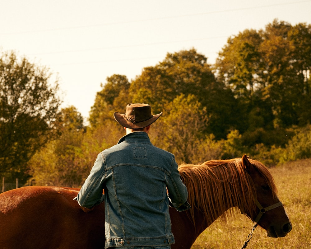 man in blue denim jacket wearing brown cowboy hat riding brown horse during daytime