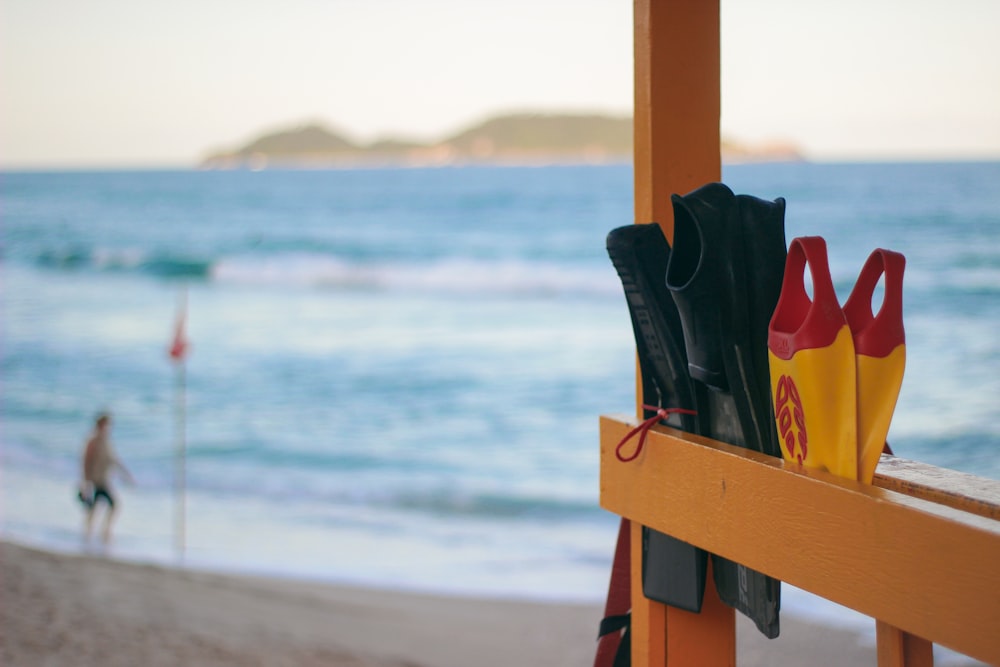 red and black leather sandals on brown wooden fence near body of water during daytime