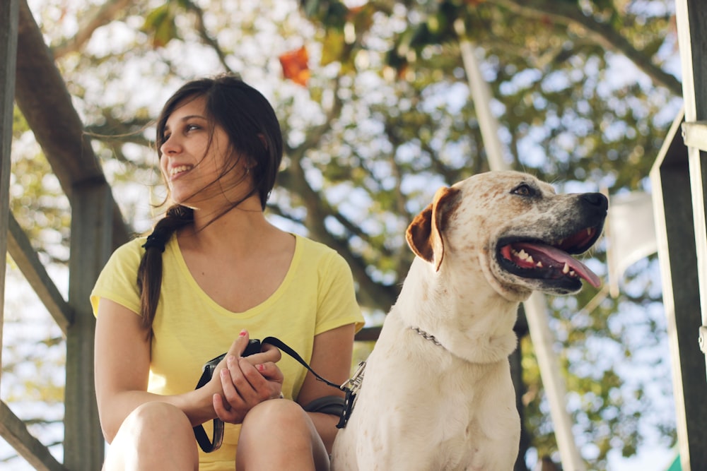 woman in yellow tank top sitting beside white short coated dog