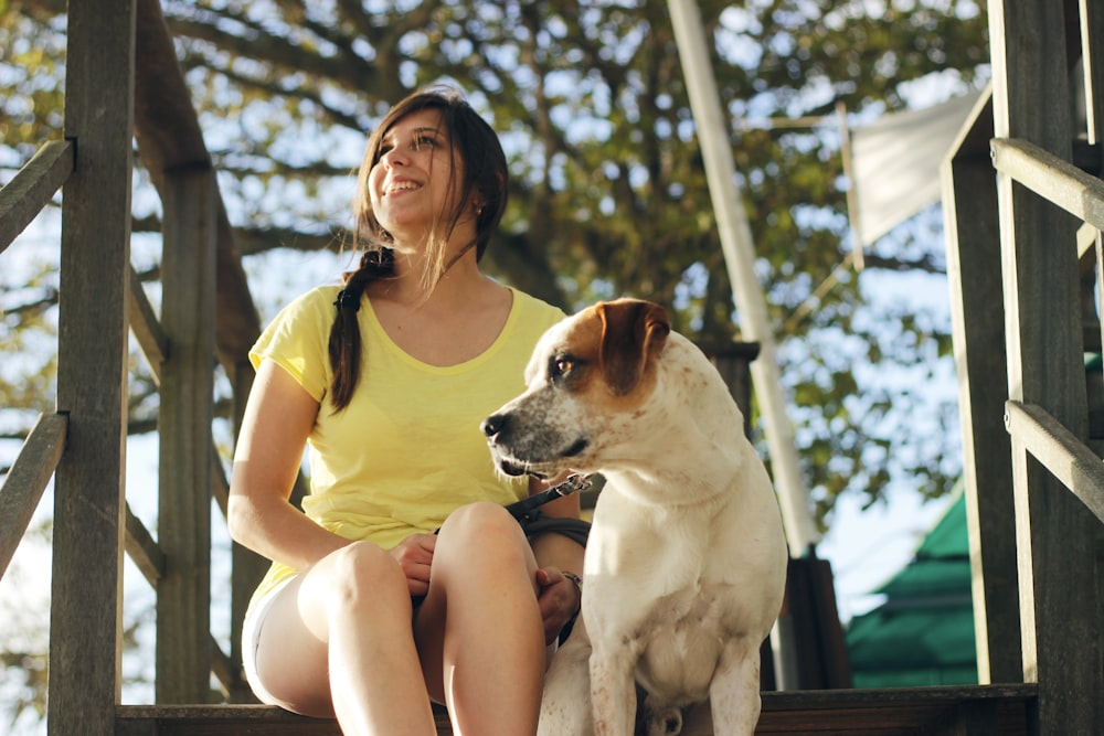 woman in yellow shirt sitting beside white and brown short coated dog