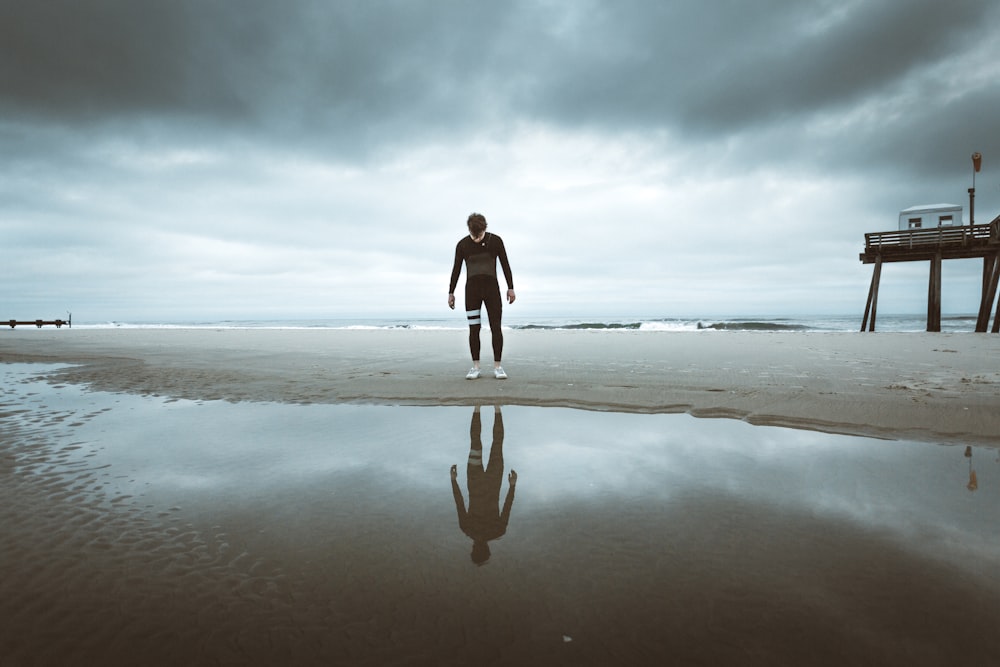 woman in black long sleeve shirt and black pants walking on seashore during daytime