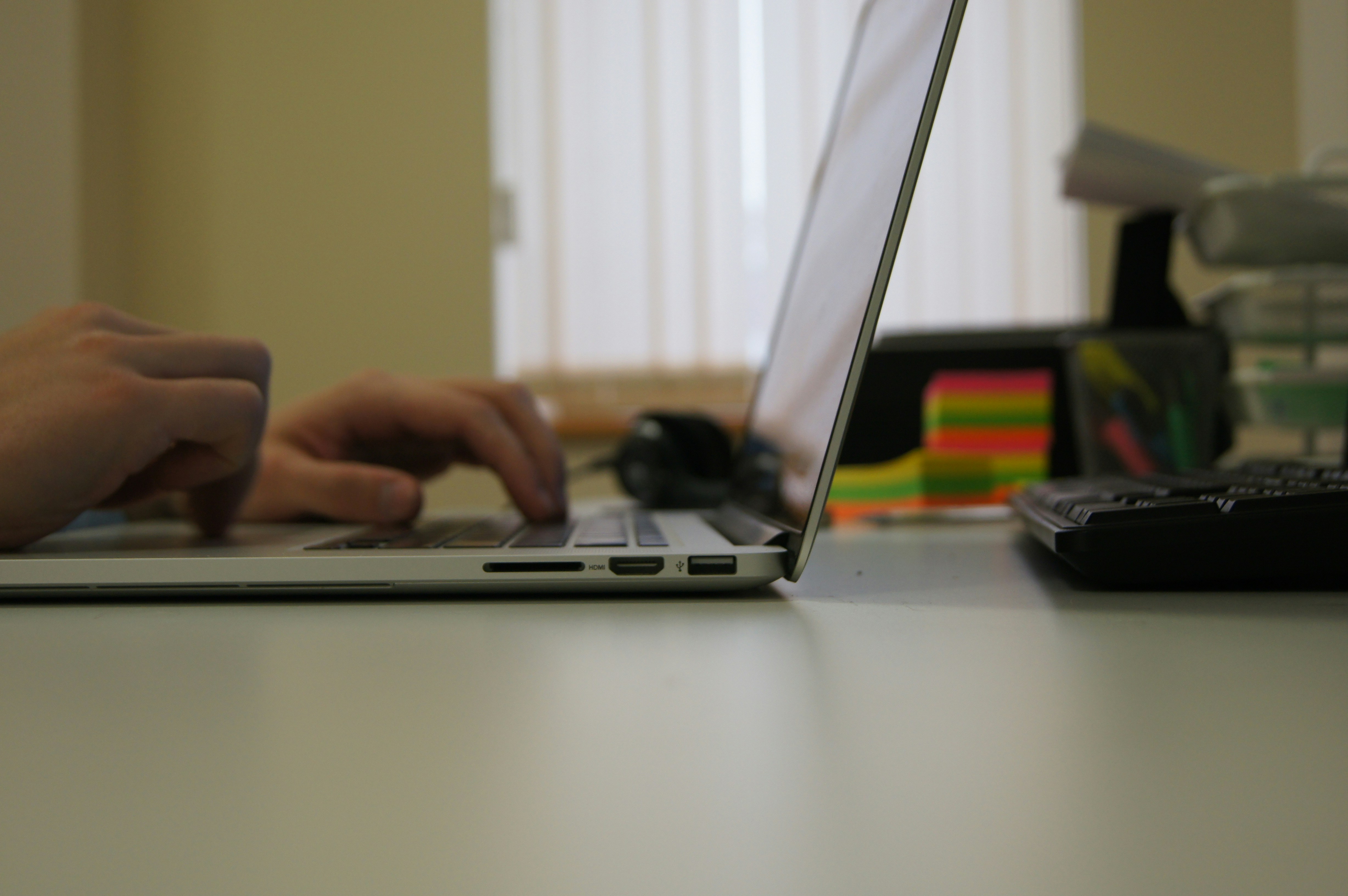 Manos escribiendo en teclado de laptop sobre escritorio blanco y ordenado
