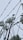 A collection of telecommunication towers with numerous satellite dishes and antennas is seen through barbed wire. The sky is overcast, creating a backdrop of gray clouds, emphasizing the industrial and slightly ominous atmosphere.