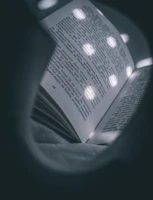 Close-up of the onwave bookmark emitting warm amber light clipped on a book page in a dimly lit room.