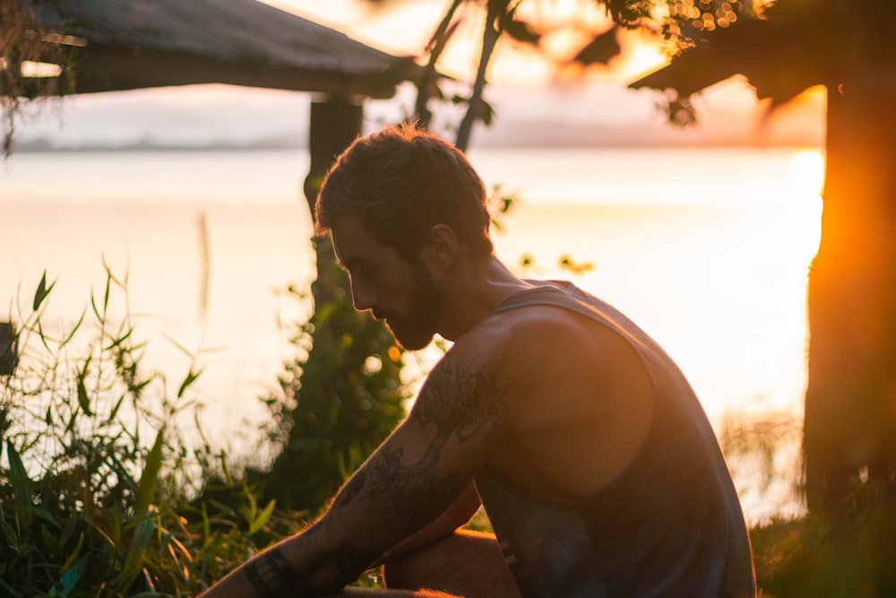 man in black tank top sitting on brown wooden bench during daytime