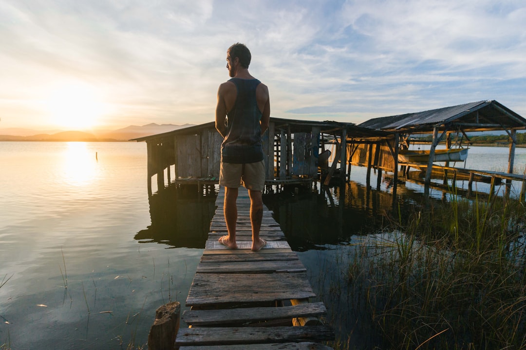 woman in white tank top and blue denim shorts standing on wooden dock during daytime