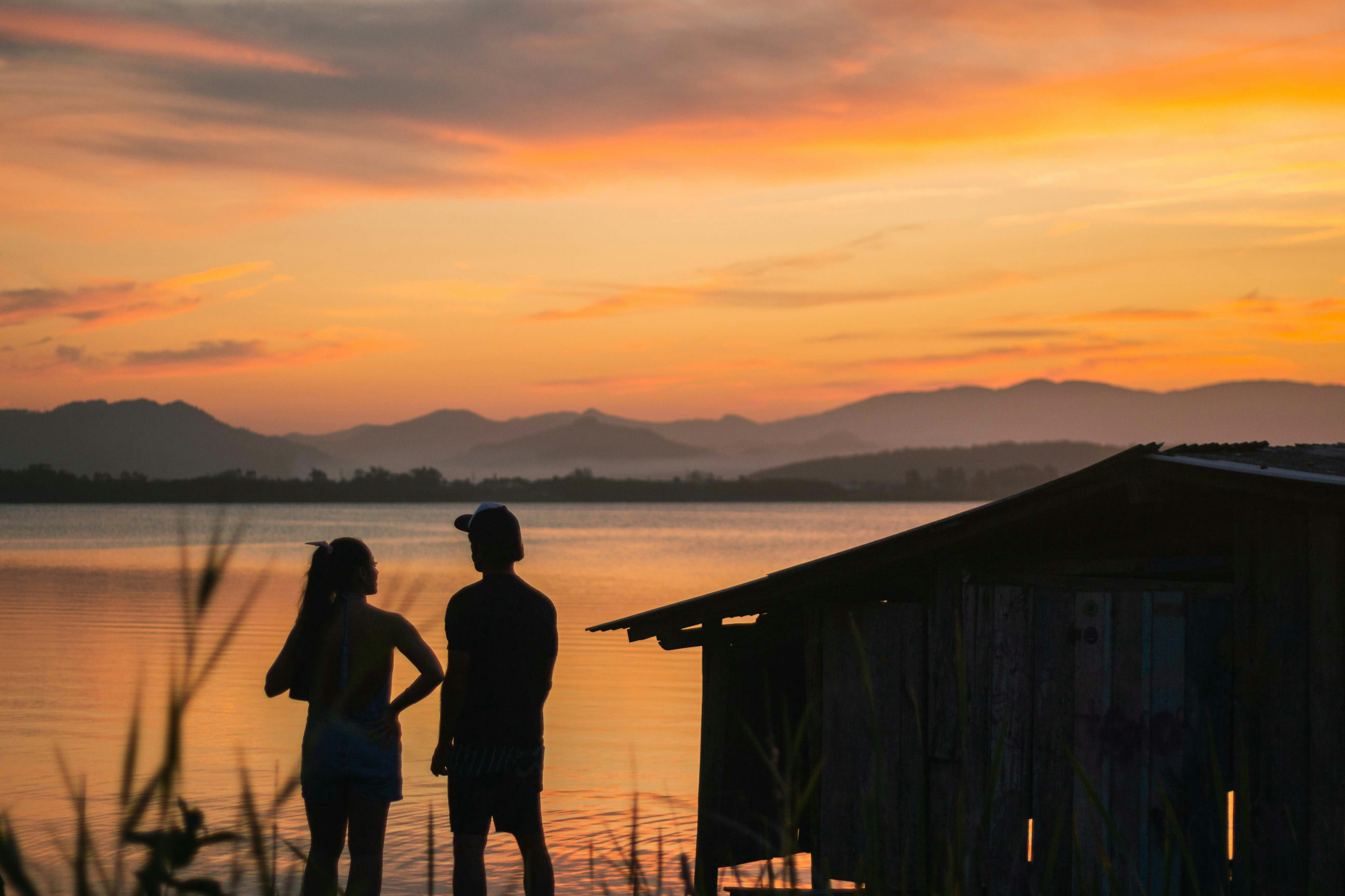 silhouette of 2 women standing on wooden dock during sunset