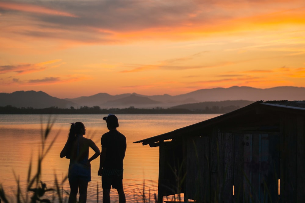 silhouette of 2 women standing on wooden dock during sunset