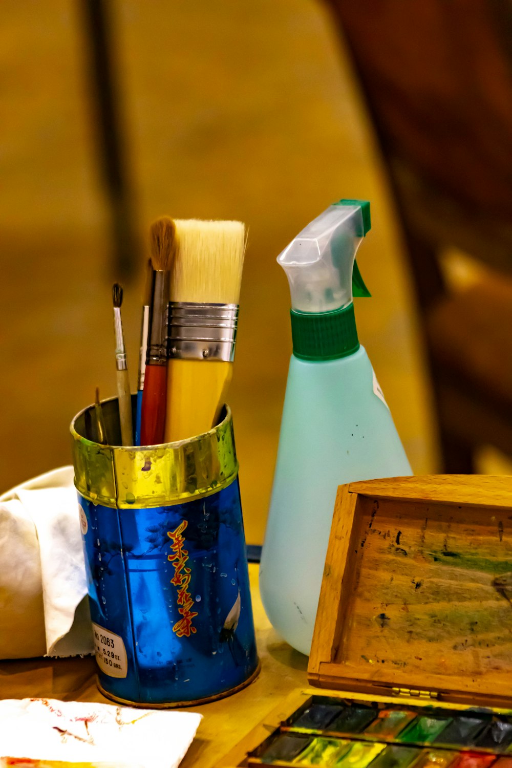 a wooden table topped with a blue bucket filled with paint and brushes