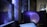 Several computer screens are displaying digital art and animations, including swirling galactic visuals and geometric designs. The atmosphere is futuristic and artistic, enhanced by ambient lighting. Various objects such as bottles and figurines appear in the background, creating an eclectic and creative environment.