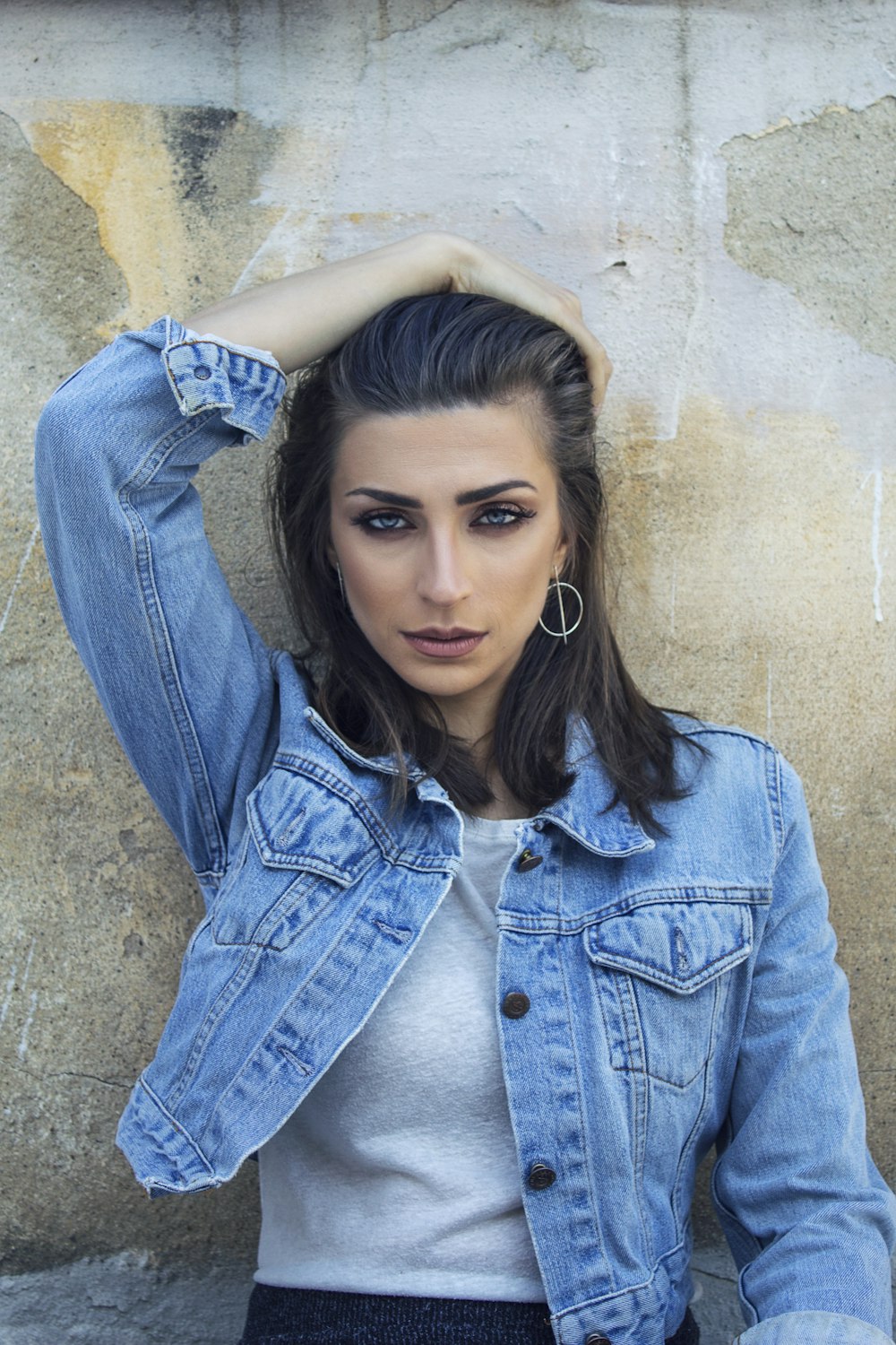 woman in blue denim button up jacket leaning on brown wall