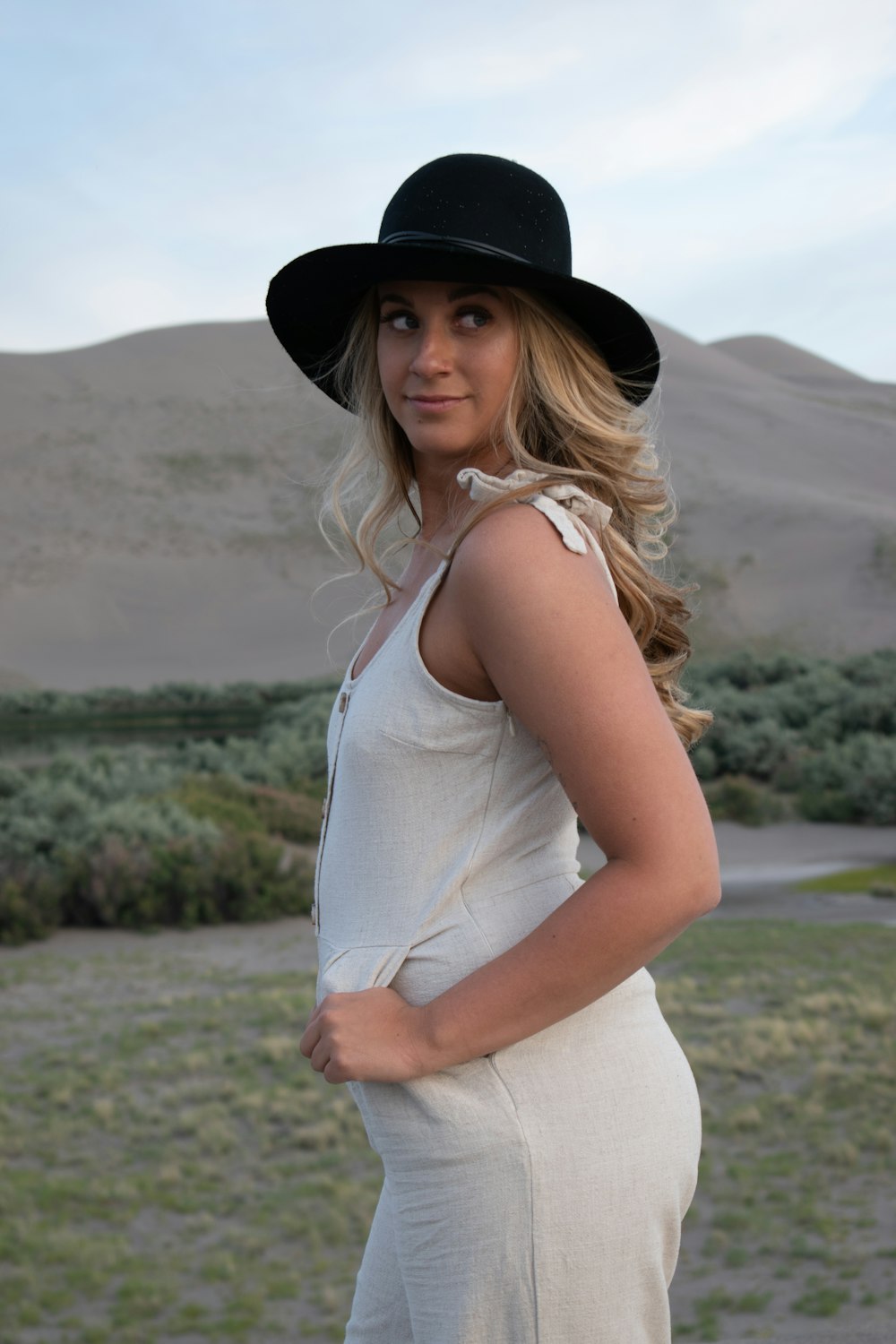 woman in white tank top and black fedora hat standing on green grass field during daytime