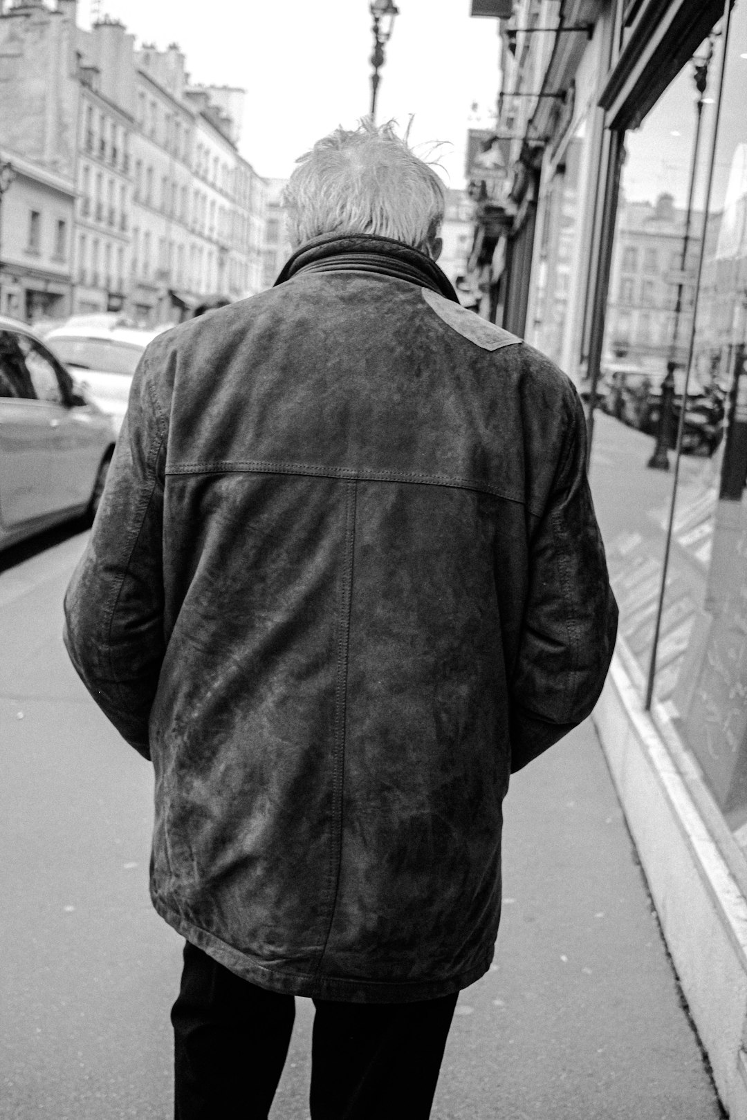 grayscale photo of man in jacket standing on sidewalk