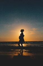 silhouette of woman standing on beach during sunset