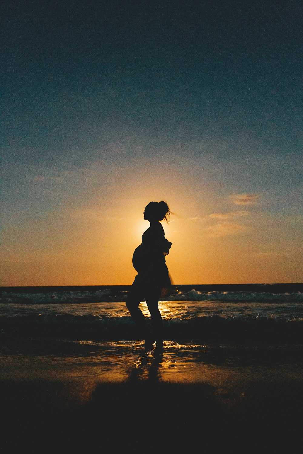 Silhouette einer Frau, die während des Sonnenuntergangs am Strand steht