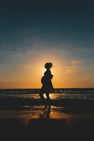 silhouette of woman standing on beach during sunset