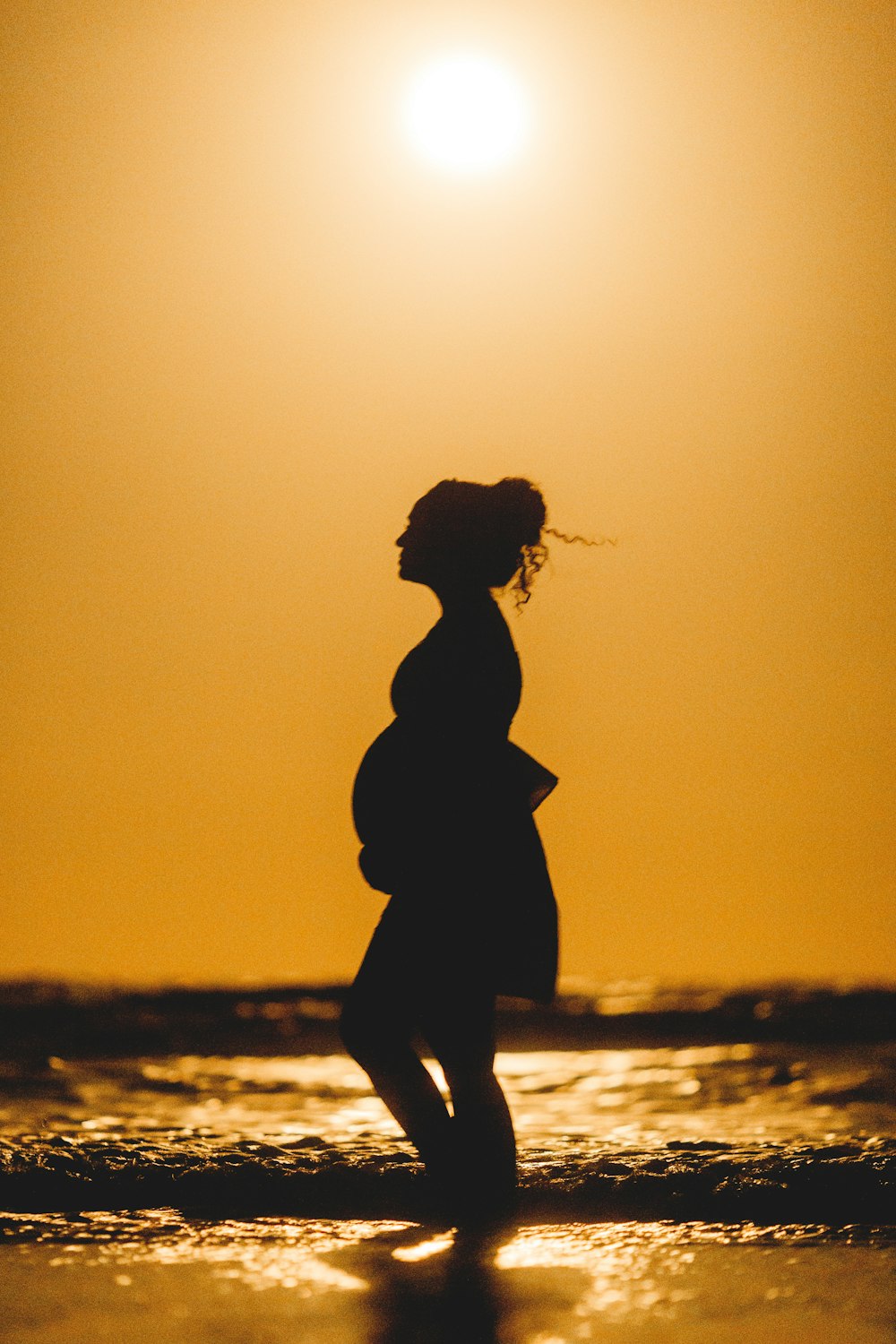 silhueta da mulher em pé na praia durante o pôr do sol