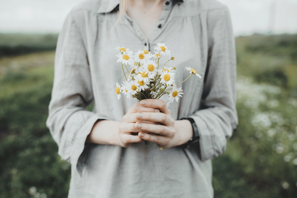 흰색과 노란색 꽃을 들고 회색 긴 소매 셔츠를 입은 여자