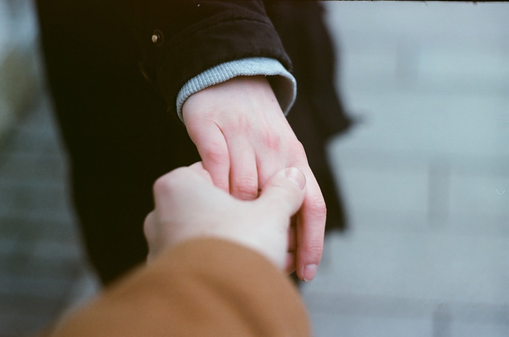 person in black long sleeve shirt holding babys hand
