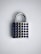 A silver padlock with a rectangular body and a curved shackle sits against a light background. The front of the padlock is adorned with rows of small, circular blue gems, giving it a decorative appearance.