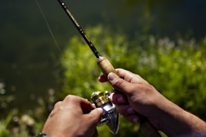 An angler's hand holding a fishing rod with a sharp fish hook ready to cast.