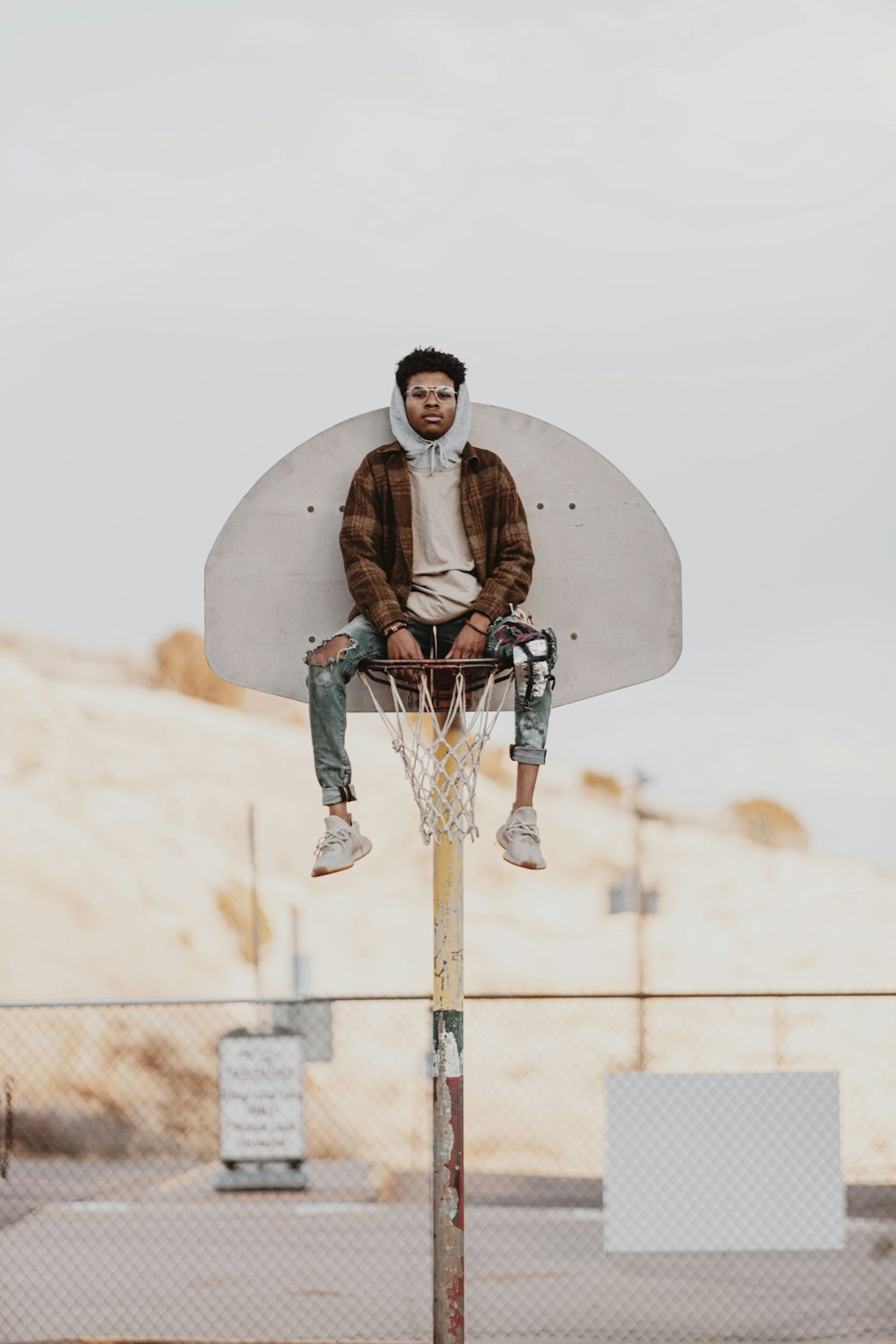 man in brown jacket and black pants sitting on white concrete wall during daytime