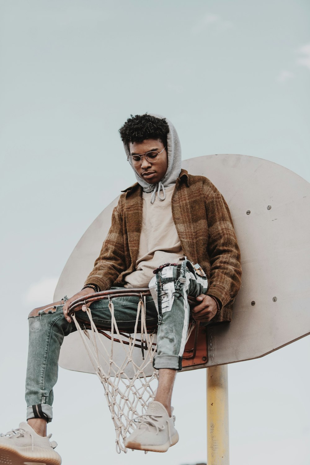 man in brown and white sweater and blue denim jeans holding white basketball hoop