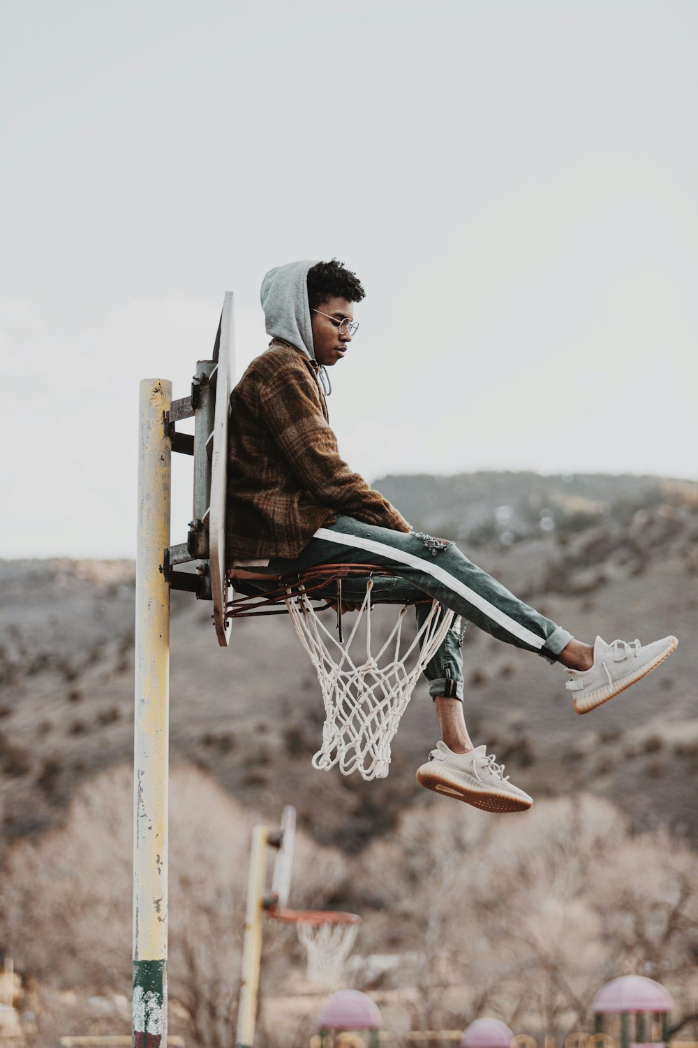 man in brown jacket sitting on basketball hoop during daytime