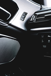 The interior of a modern car featuring sleek designs and controls. The image captures a brushed metal panel with buttons, an air vent with a glossy black finish, and part of the car's dashboard displaying text like 'BRANK HOLD'.