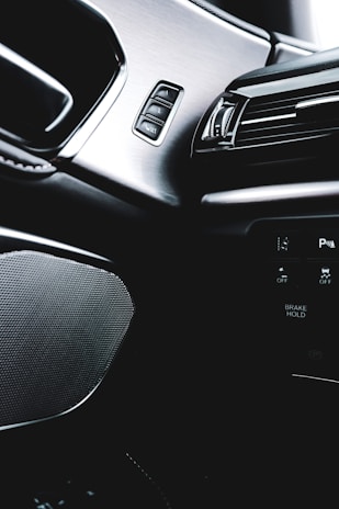 The interior of a modern car featuring sleek designs and controls. The image captures a brushed metal panel with buttons, an air vent with a glossy black finish, and part of the car's dashboard displaying text like 'BRANK HOLD'.