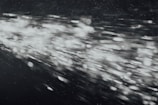 A dynamic burst of light particles streaks across a dark background, creating an abstract and energetic visual effect. The particles appear to be moving at high speed, with varying intensities and sizes, giving the image a sense of motion and depth.