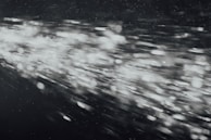 A dynamic burst of light particles streaks across a dark background, creating an abstract and energetic visual effect. The particles appear to be moving at high speed, with varying intensities and sizes, giving the image a sense of motion and depth.