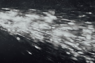 A dynamic burst of light particles streaks across a dark background, creating an abstract and energetic visual effect. The particles appear to be moving at high speed, with varying intensities and sizes, giving the image a sense of motion and depth.