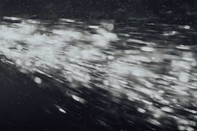 A dynamic burst of light particles streaks across a dark background, creating an abstract and energetic visual effect. The particles appear to be moving at high speed, with varying intensities and sizes, giving the image a sense of motion and depth.