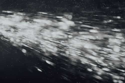 A dynamic burst of light particles streaks across a dark background, creating an abstract and energetic visual effect. The particles appear to be moving at high speed, with varying intensities and sizes, giving the image a sense of motion and depth.