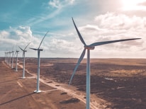 wind turbines on brown sand under white clouds and blue sky during daytime