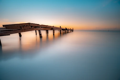 A cinematic shot of a wooden pier extending into calm waters at sunset.