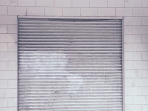 Technician repairing a metal shutter on a storefront with tools in hand.