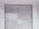 A metal roll-up shutter door is closed against a tiled wall. The door features horizontal slats and shows signs of wear and weathering. The wall consists of rectangular white tiles with a slightly worn appearance.