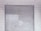 A metal roll-up shutter door is closed against a tiled wall. The door features horizontal slats and shows signs of wear and weathering. The wall consists of rectangular white tiles with a slightly worn appearance.