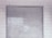 A metal roll-up shutter door is closed against a tiled wall. The door features horizontal slats and shows signs of wear and weathering. The wall consists of rectangular white tiles with a slightly worn appearance.