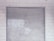 A metal roll-up shutter door is closed against a tiled wall. The door features horizontal slats and shows signs of wear and weathering. The wall consists of rectangular white tiles with a slightly worn appearance.