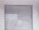 A metal roll-up shutter door is closed against a tiled wall. The door features horizontal slats and shows signs of wear and weathering. The wall consists of rectangular white tiles with a slightly worn appearance.